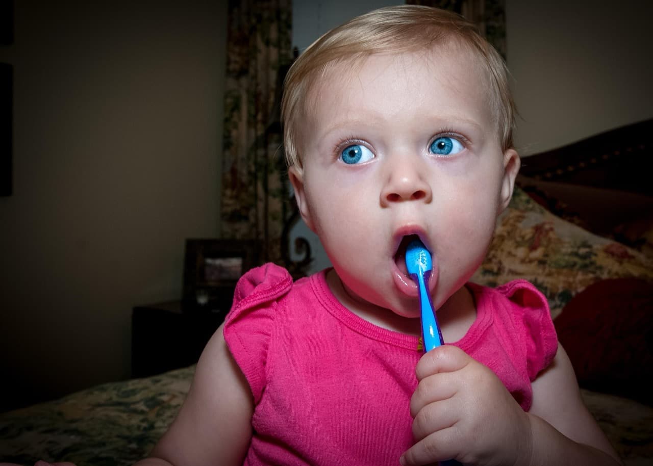 Baby holding a blue toothbrush, learning to brush teeth