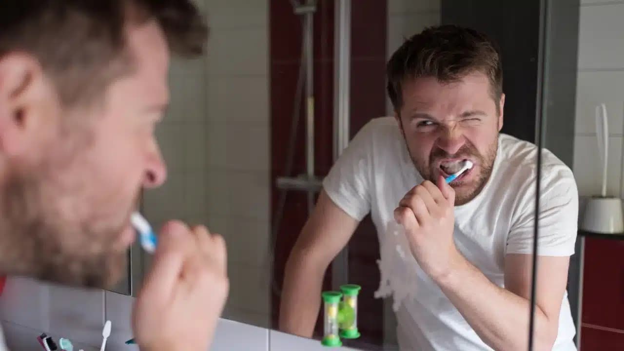 Man brushing teeth carefully in the mirror after a dental procedure