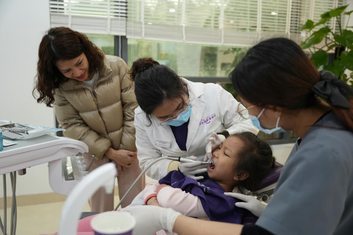 Young child getting dental exam with parent watching nearby