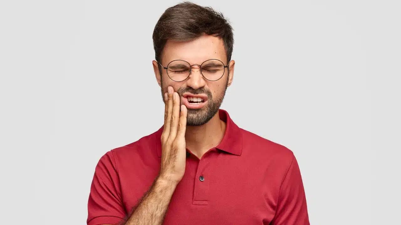 Man holding his jaw in pain, wearing glasses and a red polo shirt