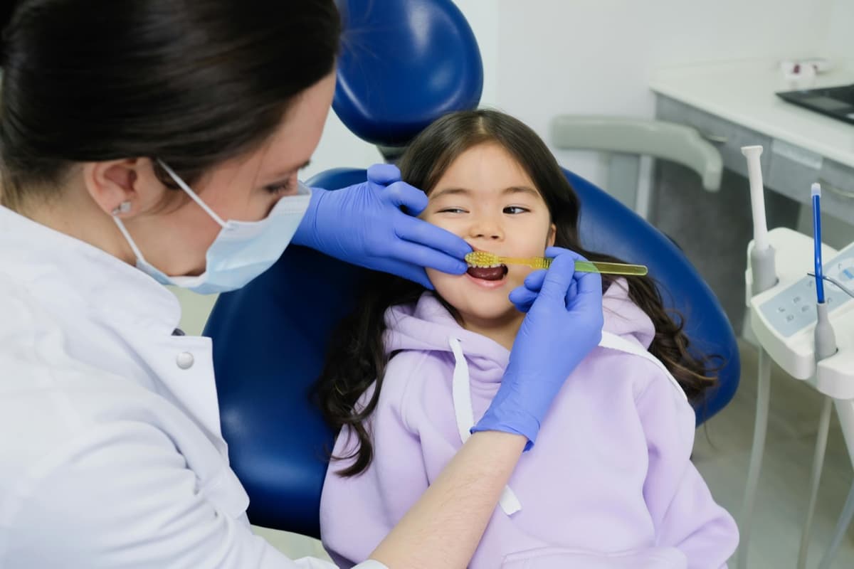 Female dentist showing a young girl proper brushing technique in the dental chair
