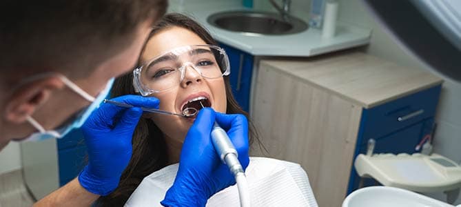 Woman in dental chair wearing safety goggles while dentist performs a root canal procedure