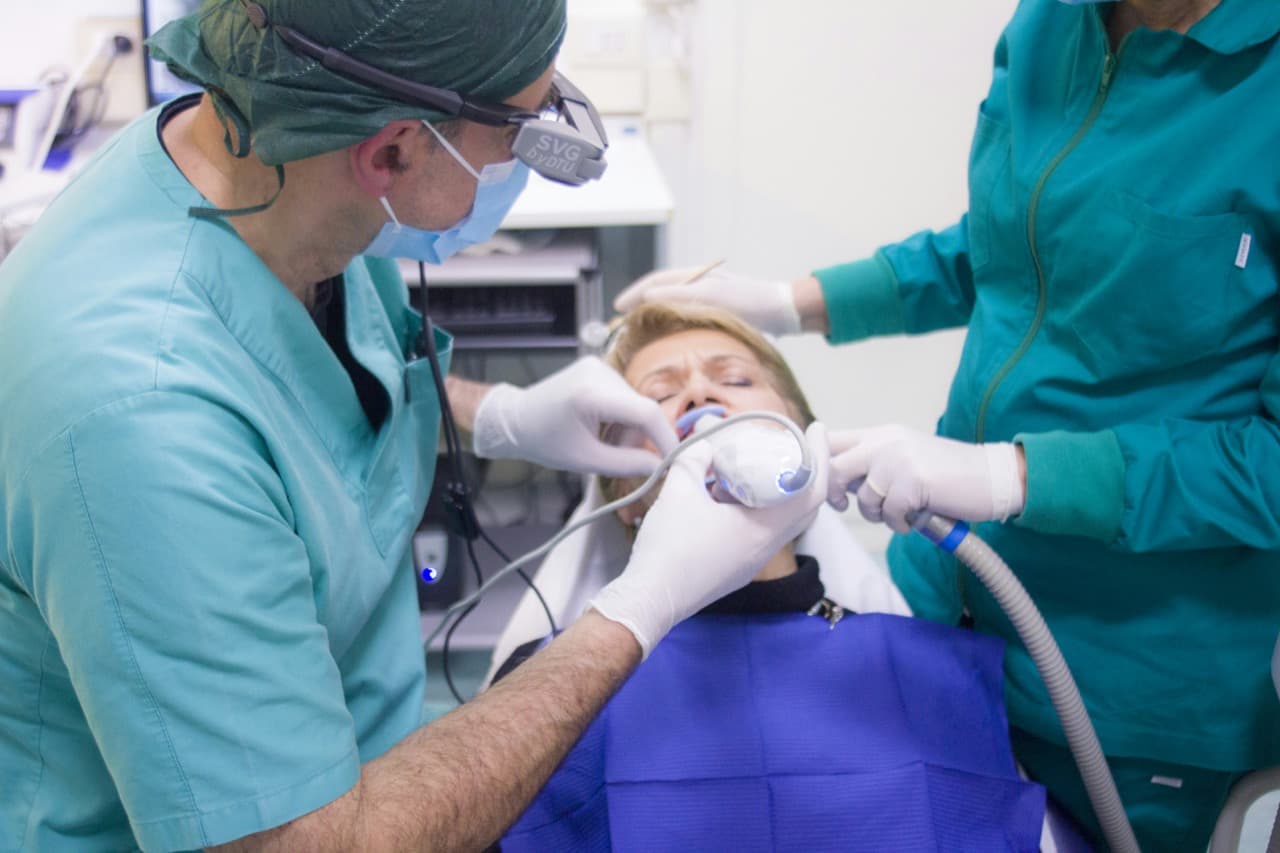 Dental team in scrubs performing wisdom teeth extraction on patient