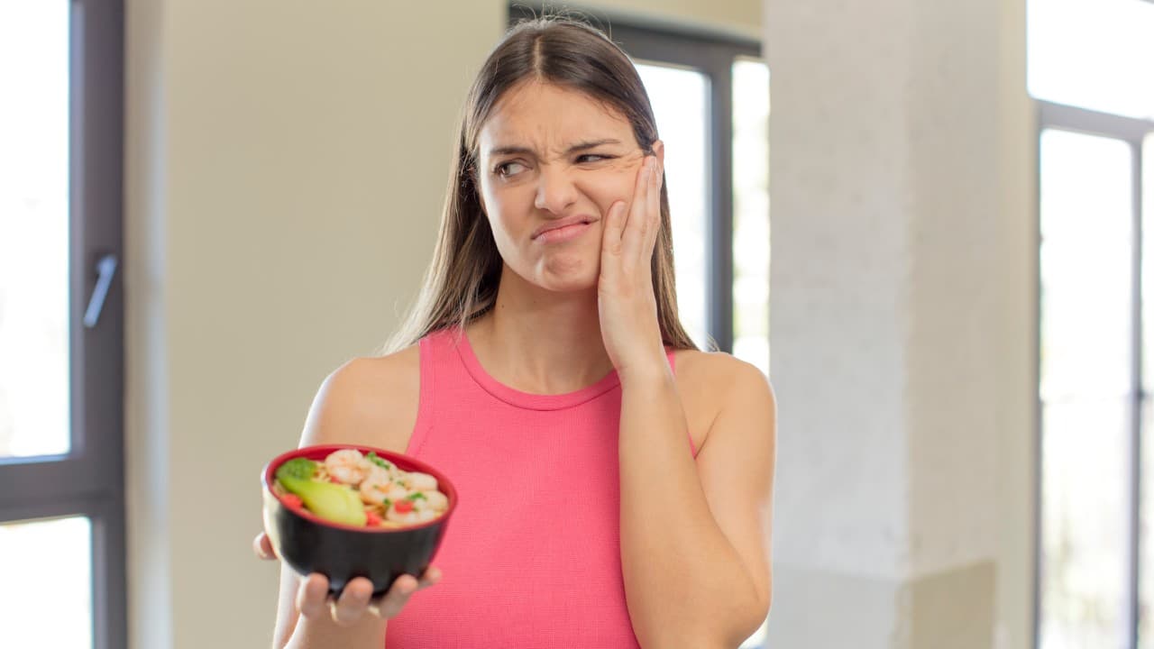 Woman holding jaw in discomfort while looking at a bowl of food