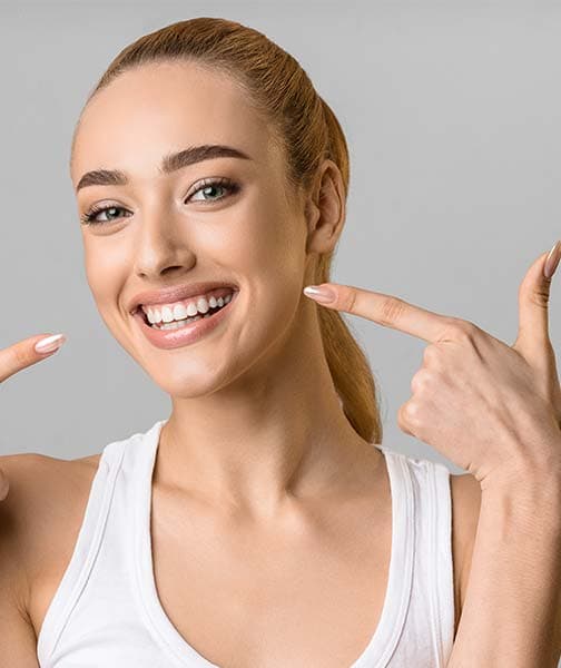 Young woman pointing at her bright white smile against a gray background